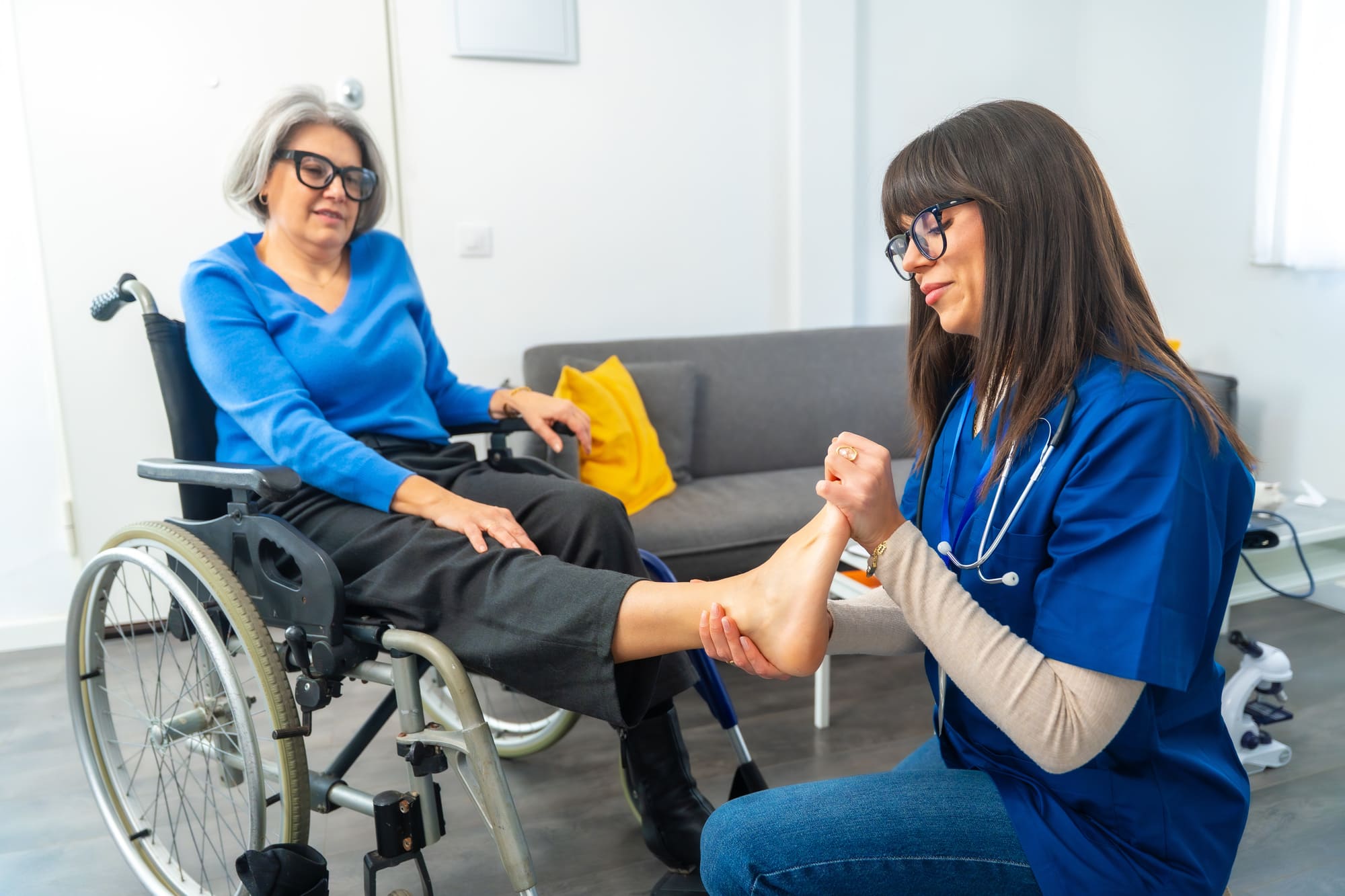 Une infirmière en soins des pieds examine le pied d'une femme âgée en fauteuil roulant.